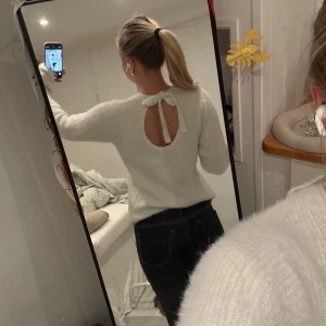 Vit stickad tröja med knyt i ryggen - Superfin vit stickad tröja med lång ärm och rund hals. Baksidan har en snygg öppning med knytband upptill som ger en extra detalj. Mjuk och fluffig känsla, perfekt för att hålla sig varm och ändå se stylish ut.