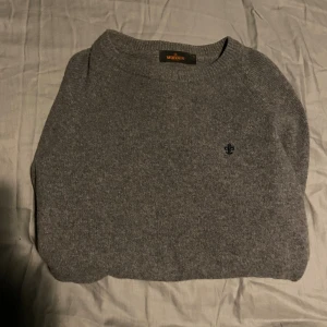 Grå stickad tröja från Morris - Säljer en stilren grå stickad tröja från Morris med rund halsringning och diskret broderad logga på bröstet. Tröjan har lång ärm och ribbade muddar för en klassisk look. Perfekt för lager-på-lager under kyliga dagar.kontakta för fler frågor eller bilder !