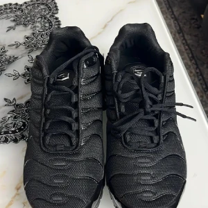 Nike Air Max svarta sneakers strl 42 - Svarta Nike Air Max sneakers med vågigt mönster och mesh-överdel. Snygga detaljer i blankt syntet och klassisk Air Max-sula för extra komfort. Rund tå, snörning och platt sula. Perfekt för dig som gillar streetstyle och sportig vibe.