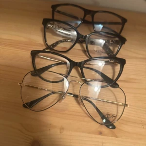 Svarta och guldiga glasögon Ray-Ban - Fyra par glasögon säljes, varav ett par är Ray-Ban med tunn guldig metallbåge och rund form. De andra har svarta, rektangulära plastbågar med stilren design. Perfekt för dig som vill ha klassiska och trendiga märkes  bågar. Säljer alla rör ett pris eller st för 500kr