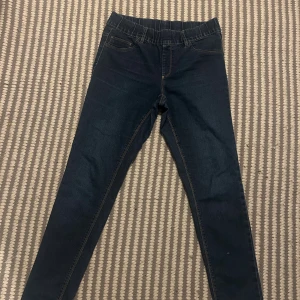 Mörkblå skinny jeans från KappAhl - Snygga mörkblå jeans från KappAhl i storlek 40 med skinny passform och elastisk midja. Klassisk femficksdesign, kontrastsömmar och mjukt stretchigt jeansmaterial som sitter skönt hela dagen. Perfekt för dig som gillar en smal siluett.