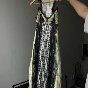 Glenn Martens x H&M långklänning - Unik långklänning från Glenn Martens x H&M med grafiskt svartvitt mönster, inslag av beige och ljusgult samt svarta spetsdetaljer vid urringningen. Klänningen har smala axelband och en cool, modern look. Perfekt för dig som vill sticka ut.