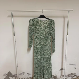 Grön mönstrad långklänning från MNG - Säljer en långklänning från MNG med grönt och vitt bladmönster. Klänningen har rund halsringning och långa ärmar med lätt puff vid axlarna. Materialet är mjukt och lätt, perfekt för dig som gillar en flowy och bekväm stil.