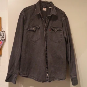Mörkgrå Levi's skjorta i bomull XL - Snygg mörkgrå skjorta från Levi's i 100% bomull, storlek XL. Klassisk westernstil med två bröstfickor med knappar och markerad krage. Långärmad med knappar vid ärmslut och fram. Perfekt för dig som gillar avslappnad och cool look.