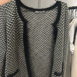 Svartvit mönstrad kofta från M&S Woman - Säljer en svartvit kofta från M&S Woman med coolt grafiskt mönster och fluffiga svarta kanter. Koftan är stickad och har lång ärm, perfekt för dig som gillar att sticka ut med din stil. Snygga fickdetaljer framtill och rund halsringning.