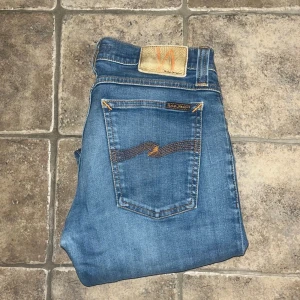 Nudie Jeans  - Säljer ett par blå Nudie Jeans Tight Long John Jeansen har klassisk femficksdesign, orangea sömmar och är tillverkade i stretchig bomullsdenim. Snygg skinny passform och ikonisk Nudie-brodyr på bakfickorna. Midja 35cm, längd 101cm.  Ifall det inte finns någon bild i annonsen där jag bär plaggen jag säljer så är det för att jag ej kan ha storleken heller passformen, så kolla måtten för storlek och googla på modellnamnet för passform 😉 s4