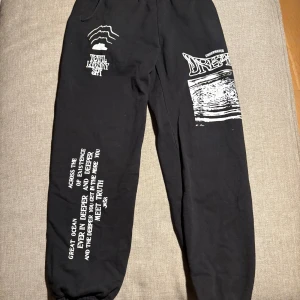 Svarta mjukisbyxor från Total Luxury spa. - Svarta mjukisbyxor från Total Luxury Spa med vita grafiska tryck och textdetaljer på benen. Byxorna har resår i midjan och vid bensluten, samt en bakficka. Sköna och avslappnade med unik design och coola prints.