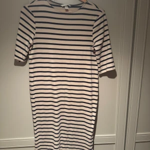 Randig tshirtklänning från H&M Mama - Snygg tshirt klänning från H&M Mama med klassiskt marinblått och vitt randigt mönster. Klänningen har rund halsringning och korta ärmar, tillverkad i mjuk bomull som känns skön mot huden. Perfekt för dig som gillar enkel och stilren design. Slits detalj längst ner.