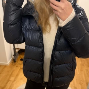 Svart dunjacka från Colmar med huva - Snygg svart dunjacka från Colmar med huva och dragkedja framtill. Jackan har en puffad  och logotyp på ärmen. Perfekt för kalla dagar, Den är i italiensk storlek men den sitter som en M-L, jätte bra skick, säljer för vill köpa sen annan jacka nu 💖💖pris kan diskuteras och kvitto finns 💓