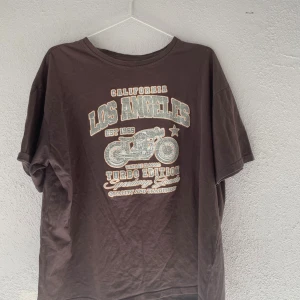 Brun Los Angeles t-shirt från SHEIN - Cool brun t-shirt från SHEIN med tryck i vitt och beige som visar en motorcykel och texten 'Los Angeles California Turbo Edition'. T-shirten har rund hals och korta ärmar, tillverkad i 100% bomull för skön känsla. Perfekt för dig som gillar streetstyle och vintagevibbar.