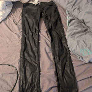 Svarta skinn skinny jeans från Vero Moda - Svarta skinny jeans från Vero Moda med coated finish som ger en cool läderlook. Byxorna har dragkedjor på bakfickorna och klassisk femficksdesign. Passformen är tight och midjan är normal. Perfekt för dig som gillar en edgy stil.