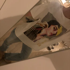 Vit t-shirt med grafiskt tryck - Vit t-shirt från Zara med ett stort grafiskt tryck framtill som visar en person med färgglada detaljer och mönstrad jacka. T-shirten har rund hals och korta ärmar, och är gjord i mjuk bomull. Passformen är loose och trycket har coola färginslag som gul, svart och röd. 