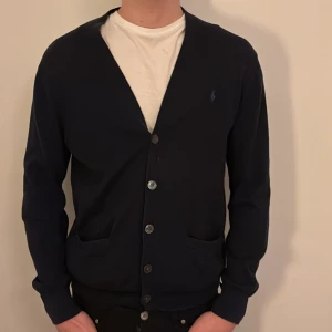  Ralph Lauren Mörkblå kofta - Snygg mörkblå kofta från Ralph Lauren med klassisk v-ringning och knappar framtill. Tröjan har två fickor och diskret broderad logga på bröstet. Perfekt för lager-på-lager och passar till det mesta. ALDRIG ANDVÄND PRISET ÄR DISKUTERBART