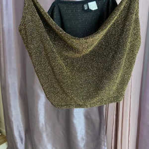 Glittrig guld croppad linnetopp H&M - Säljer en glittrig croppad linnetopp från H&M DIVIDED i guld med tunna svarta axelband. Toppen har en snygg draperad v-ringad front och är perfekt för att sticka ut. Materialet är syntet med glittriga trådar som ger en cool effekt. Passar dig som gillar att glänsa.