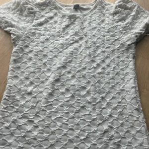 Vit blus med struktur från shein  - Säljer en vit blus från shein i storlek XS. Toppen har ett unikt strukturerat tyg med upphöjda detaljer över hela ytan och rund hals. Kortärmad och i ett mjukt, syntetiskt material som känns skönt mot huden. Perfekt för dig som gillar coola texturer!