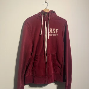 Abercrombie & Fitch vinröd hoodie, storlek XLARGE - Vinröd hoodie med dragkedja från A&F New York. Hoodien har två fickor fram och dragsko.   Skick: Mycket gott skick, sparsamt använd utan defekter.   Storlek: XL  Kolla gärna in mina andra annonser.   Skriv vid frågor eller ifall du vill ha fler bilder. 