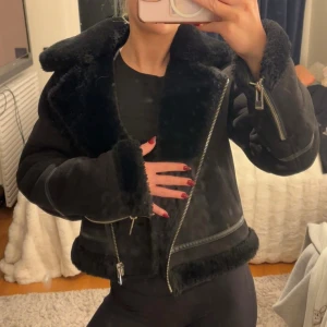 Svart teddyjacka från Pull&Bear - Säljer en svart jacka från Pull&Bear i storlek S. Jackan har fluffig krage och muddar, tvåvägsdragkedja framtill och detaljer i syntetmaterial. Croppad modell med snygga sömmar och lång ärm, perfekt för att ge din outfit edge.