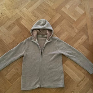 Beige stickad cardigan från Reserved - Säljer en beige stickad cardigan från Reserved med dragkedja framtill. Tröjan har en mjuk huva med beige innerfoder och långa ärmar. Perfekt för lager-på-lager och chill dagar pris är ej hugget i sten så kom men era pris