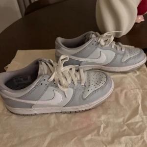 Nike Dunk Low ljusgrå sneakers - Nike Dunk Low sneakers i ljusgrått och vitt med klassisk snörning. Snygg låg modell, perfekt för dig som gillar cleana och stilrena sneakers. Använt dom ett tag men dom är fortfarande i bra skick och går att tvätta. Skorna passar 38/39. Pris kan diskuteras!
