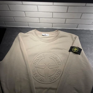 Beige Stone Island sweatshirt - Snygg beige sweatshirt från Stone Island med stort broderat logomärke på bröstet och klassisk patch på ärmen. Tröjan är använd mycket lite och är i väldigt bra skick det är XXL men passar ungefär som L. Lappen Med QR kod följer även med i paketet