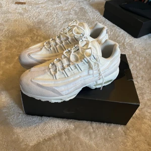 Nike Air Max 95 vita sneakers CDG - Nike Air Max 95 sneakers i helvitt med inslag av ljusgrått. Skorna har en chunky sula med synliga Air-enheter, mesh och mockadetaljer samt snörning framtill. Perfekt för dig som gillar en clean och sportig look.
