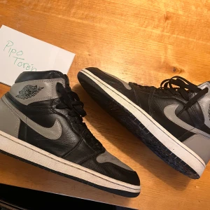 Nike Air Jordan 1 Shadow  - Säljer ett par klassiska Nike Air Jordan 1 Highs i färgen Shadow. Skorna har svart och grått skinn, svart snörning och den ikoniska Air Jordan-loggan på sidan. Ingen OG box och heeldrag som jag lagat. EU 42,5