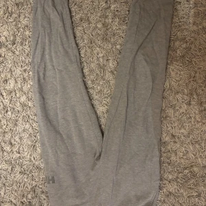 Grå mjukisbyxor från Helly Hansen - Grå mjukisbyxor från Helly Hansen med elastisk midja och diskret HH-logga på benet. Tillverkade i mjukt bomullsmaterial med insida i frotté för extra komfort. Perfekta för chill eller träning.