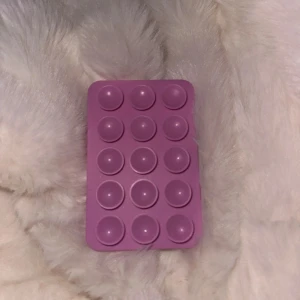 MagSafe kompatibelt popsocket-fäste - Lila MagSafe-kompatibelt popsocket-fäste för iPhone. Fästet har 12 poppande knappar för bättre grepp och stöd. Passar MagSafe-telefoner och är i fint skick utan synligt slitage. Perfekt för att hålla mobilen säkert och bekvämt. Har några rivmärken på baksidan som knappt syns.