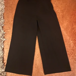 Svarta vida kostymbyxor H&M stl 36 - Svarta kostymbyxor från H&M i storlek 36. Byxorna har hög midja, vida ben och bälteshällor. Perfekta för en clean och stilren look. Materialet känns mjukt och följsamt, vilket gör dem bekväma att bära hela dagen.