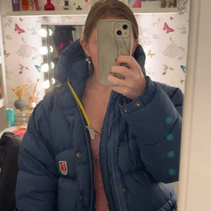  Fjällräven XXXS - Säljer en blå pufferjacka från Fjällräven i storlek XXXS. Jackan har hög krage, gul detalj vid dragkedjan och klassisk Fjällräven-logga på bröstet. Perfekt för kalla dagar och har en riktigt schysst oversized look. Jackan är i fint skick. Säljer då den är för stor. Pris kan diskuteras 