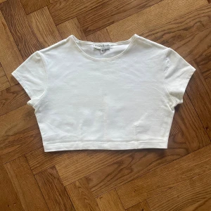 Vit croppad topp från Bebe - Säljer en vit croppad topp från Bebe i storlek S. Toppen har rund halsringning och korta ärmar, tillverkad i mjuk bomull. Enkel och clean design som är lätt att matcha med allt. Perfekt för dig som gillar minimalistisk stil.