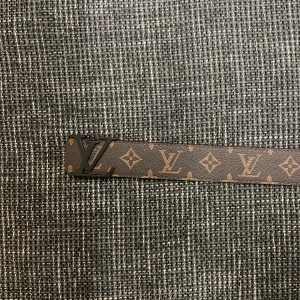 Louis Vuitton monogram bälte brun - Säljer ett brunt Louis Vuitton bälte med klassiskt monogrammönster och svart LV-spänne. Bältet är gjort i skinn och har de ikoniska LV-loggorna och blommorna tryckta längs hela remmen. Perfekt accessoar för att lyfta din outfit.