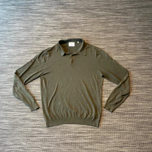 Olivgrön pikétröja från Bläck - Snygg olivgrön pikétröja från Bläck i storlek M. Tröjan har klassisk krage, två knappar vid halsen och långa ärmar. Materialet är mjukt och tunt, perfekt för lager-på-lager. Passformen är normal och tröjan har ribbade muddar vid ärmslut och nederkant.