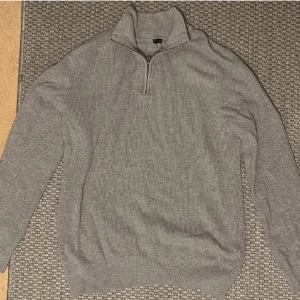 Half zip tröja - Säljer en stilren grå ribbad tröja med dragkedja i halsen. Perfekt för kyligare dagar och enkel att matcha med olika outfits.
