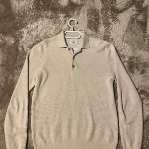 Beige pikétröja från Bläck - Snygg beige pikétröja från Bläck i storlek S. Tröjan har klassisk krage, knappar vid halsen och är långärmad. Materialet är stickat och ger en mjuk känsla. Använd ett fåtal gånger så i väldigt bra skick!