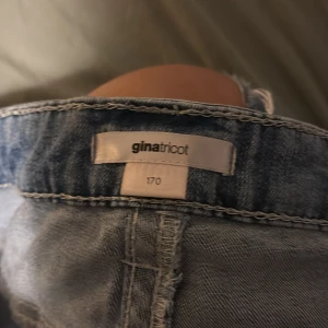 Bootcut jeans från Gina Tricot, ljusblå - Ljusblå bootcut low waist jeans från Gina Tricot i storlek 170. Jeansen har slitna detaljer framtill och snygga broderade fickor bak. Klassisk femficksmodell med knapp och dragkedja. Perfekta för dig som gillar en avslappnad men trendig look.