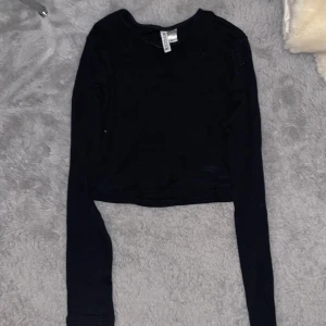 Svart croppad långärmad topp H&M - Svart långärmad cropped topp från H&M Basic, modell DIVIDED. Croppad passform med rund halsringning och mjukt, stretchigt material som sitter skönt mot kroppen. Perfekt att styla med jeans eller kjol för en clean look.
