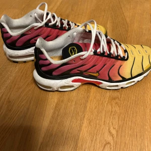 Nike Air Max Plus TN Sunset 42.5 - Nike Air Max Plus TN Sunset med grymt färgstark gradient från gul till röd och svarta detaljer. Snygga vita snören och TN-logga på plösen. Sulan har coola detaljer i svart och gult. Ovandelen är i syntetmaterial med klassisk Air Max-dämpning. Perfekt för dig som vill sticka ut.