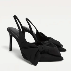 Svarta pumps med rosett från Stradivarius - Snygga svarta pumps från Stradivarius med spetsig tå och hög klack. Skorna har en stor rosett framtill och öppen häl med smal rem. Aldrig använda strl 39. ”snöret sitter kvar runt skorna med stradivarius lapp. Nypris 399