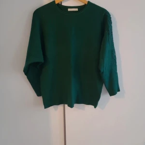 Grön tröja med broderi från An Feiya - Mörkgrön långärmad tröja från An Feiya med snyggt blommigt broderi och pärlor längs ena ärmen. Materialet är mjukt och består av 20% kashmir, 70% bomull och 10% spandex. Rund halsringning och normal passform. Perfekt för dig som gillar unika detaljer. Längd 63 bredd 53cm