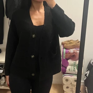 Svart kofta med stora knappar - Säljer en svart, mysig kofta med stora knappar framtill och två praktiska fickor. Koftan har långärmad design och är stickad med breda muddar vid ärmslut och nederkant. Perfekt för lager-på-lager och chill dagar.