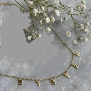 Peg x Penny x Guldfynd  - Snyggt halsband i guldton med hängande bokstäver som bildar ordet 'SISTER'. Kedjan är tunn och elegant, perfekt för att ge en personlig touch till din stil. Passar dig som vill visa lite extra kärlek till din syster.