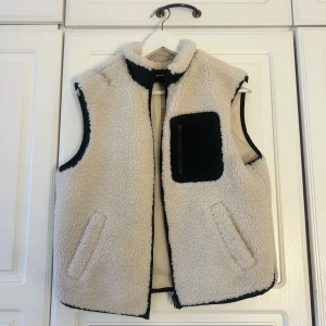 Beige väst med svart ficka💖💖 - Säljer en beige fleeceväst från Vero Moda med svart kontrastficka på bröstet och dragkedja. Västen har två sidofickor och svarta detaljer längs kanterna. Perfekt för lager-på-lager och chill stil✨✨