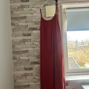 Orange långklänning med smala axelband - Säljer en orange  långklänning med smala axelband och rundad hals. Klänningen har en enkel och flowy siluett som ger en chill vibe. Materialet känns mjukt och lätt, perfekt för varmare dagar. Passar dig som gillar minimalistisk stil och vill ha något bekvämt men snyggt.