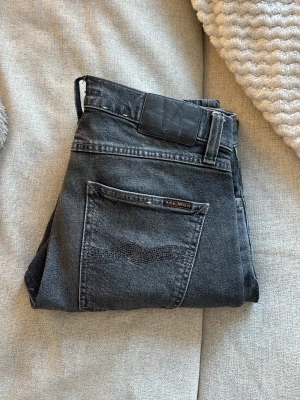 Grå raka jeans från nudie  med tvättad look - Säljer ett par nudie grå jeans med snyggt tvättad effekt och raka ben. Jeansen har klassisk femficksdesign och normal midja. Perfekta för dig som gillar en avslappnad och stilren vibe.