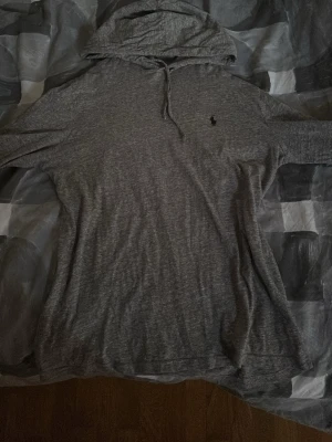 Grå hoodie från Polo Ralph Lauren - Snygg grå hoodie från Polo Ralph Lauren med klassisk huva och dragsko. Tillverkad i mjukt bomullsmaterial och har de lilla loggan broderad på bröstet. Perfekt för en chill och stilren look.