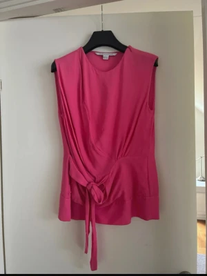 Rosa ärmlös blus från DVF - Snygg rosa ärmlös blus från Diane von Furstenberg med rund halsringning och knytning i midjan. Blusen har en feminin siluett och är perfekt för dig som gillar färg. Materialet är 100% silke