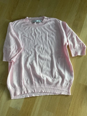 Ljusrosa tröja med kort ärm - Söt ljusrosa tröja med korta ärmar och rund hals. Tröjan är tillverkad i mjukt material och har ribbade muddar vid hals, ärmslut och nederkant. Perfekt för en enkel och stilren look.