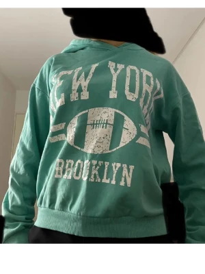 Turkos hoodie med New York-tryck - PRIS KAN DISKUTERAS💕💕💕 Turkos hoodie från Kappahl med vit text 'NEW YORK BROOKLYN' och amerikansk fotbollstryck på bröstet. Mjuk insida, huva och ribbade muddar. Långärmad och i skönt bomullsmaterial. Lite lim på armen bak men inget som märks, bild finns i annonsen! Köpt för runt 299-399 kr💕passar som S-M