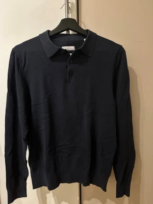 Mörkblå polotröja  - En stickad polotröja från These glory days i storlek s. Tröjan är använd men fortfarande i gott skick och har inga övriga skavanker. 